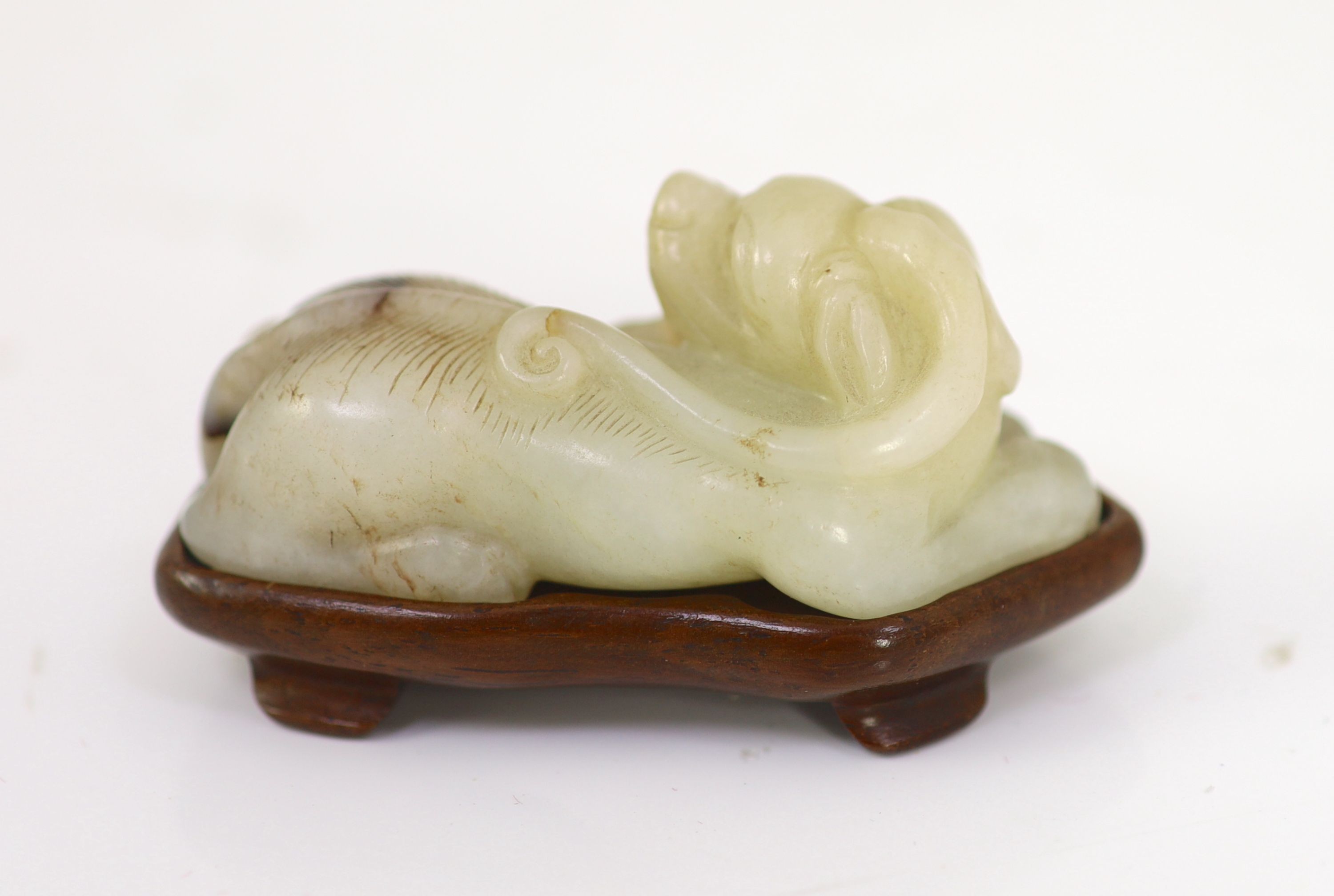 A Chinese pale celadon and brown jade figure of a lion-dog, 18th/19th century, 6.7cm long, wood stand